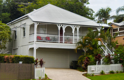 Front of a small Queenslander home with fret work and a front verandah, a drive and a white picket fence purchased by home loan brokers services