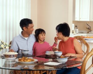 image of a dark haired family - mother, father and daughter - sitting around a glass table in their kitchen sharing food for mortgage refinancing