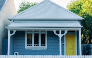 image of a small blue cottage with a bright yellow door and white picket fence demonstrating residential real estate investing