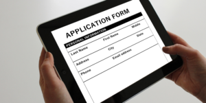 graphic of hands holding black and white first home guarantee scheme application form on a tablet