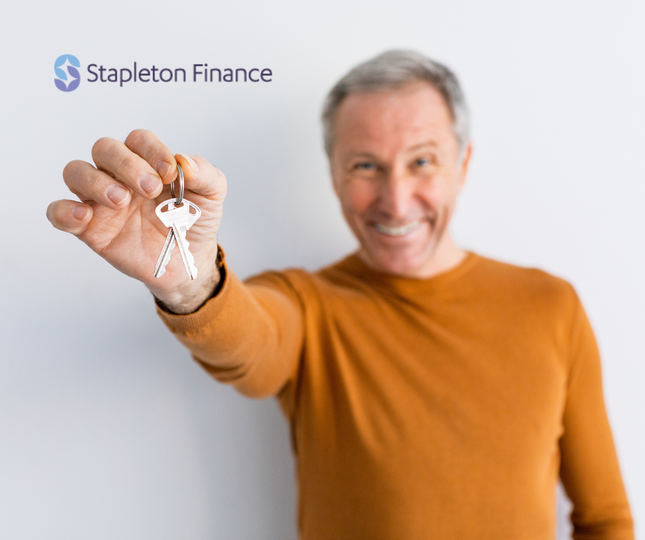 image of a smiling older man in a mustard coloured shirt holding out a key with the Stapleton Finance logo in the corner for home loans for older borrowers