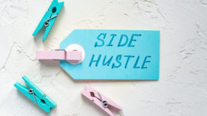 image of blue paper with the words side hustle written on it held by a pink clothespin with blue and pink clothespins scattered around it