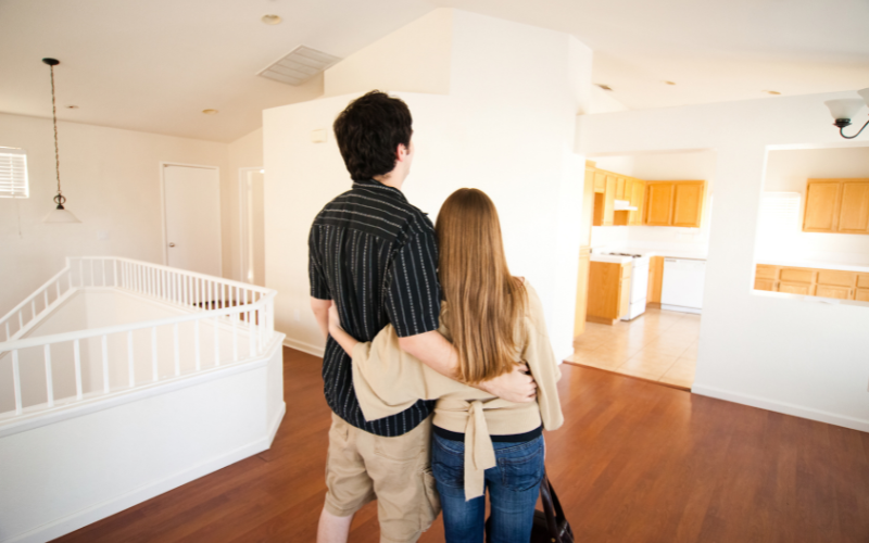 couple with their backs to camera and arms around each other looking at their first home