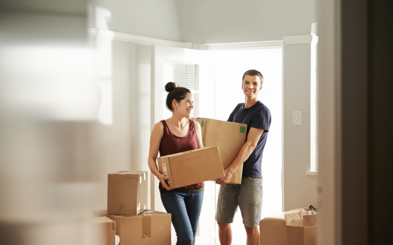 couple smiling while carrying boxes into their new first home for guide for first time home buyers 