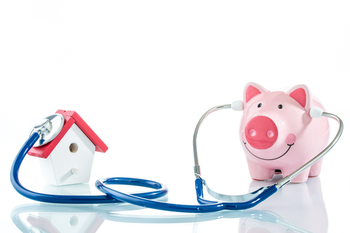 small white and red house and pink piggy bank with stethascope between them