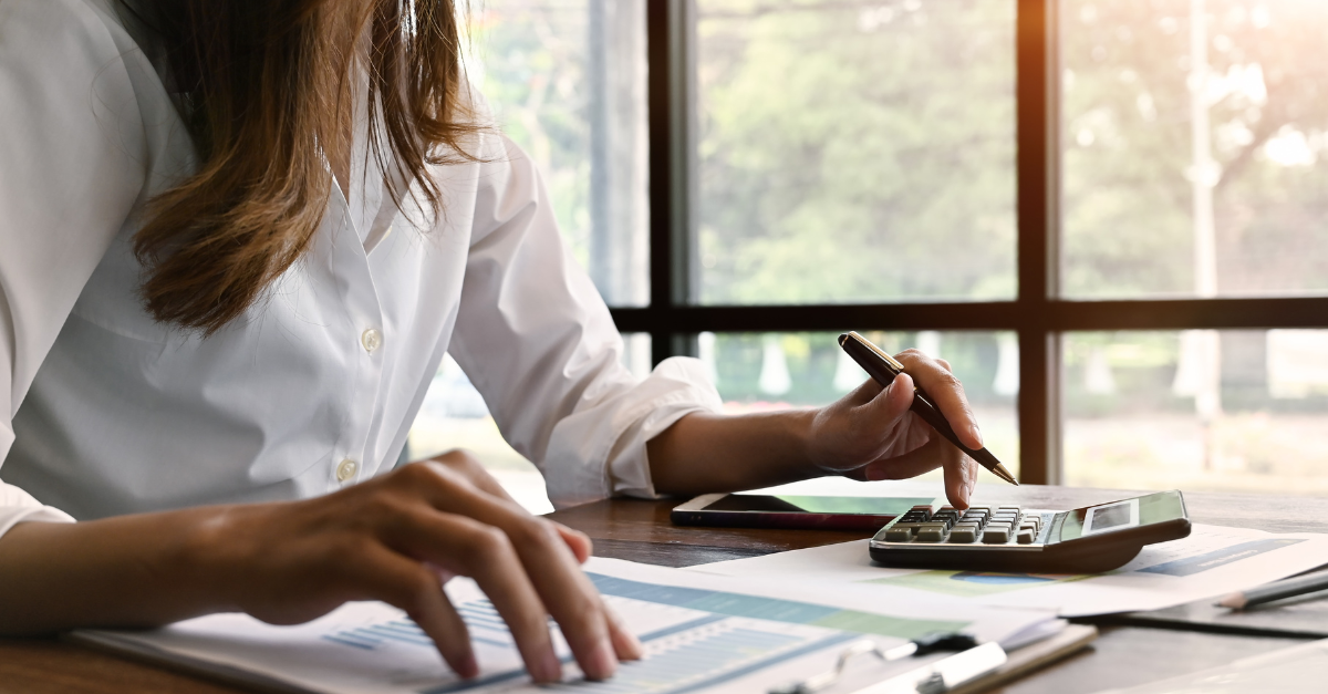 woman in white shirt sitting at desk with a pencil and a calculator to calculate her buying power