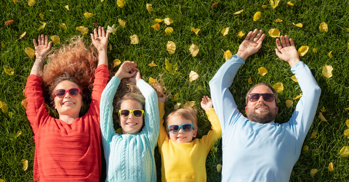 happy family in bright colours laying on the grass with their hands over their heads and smiling for home loan broker helping them with a new home