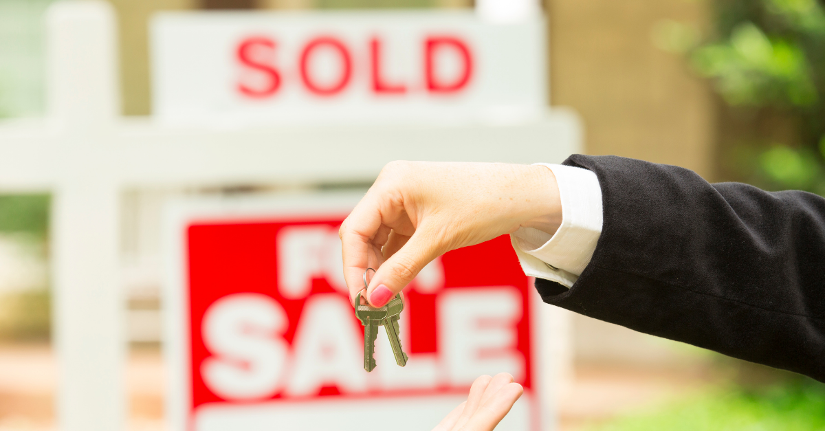 Sold sign over a for sale sign with a home loan broker holding keys to a new house