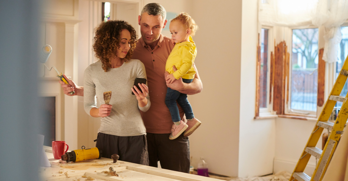 man, woman and baby standing in a room that's being renovated and holding paint brushes, discussing the renovations, for how much will i save with a rate cut and how to use that to renovate