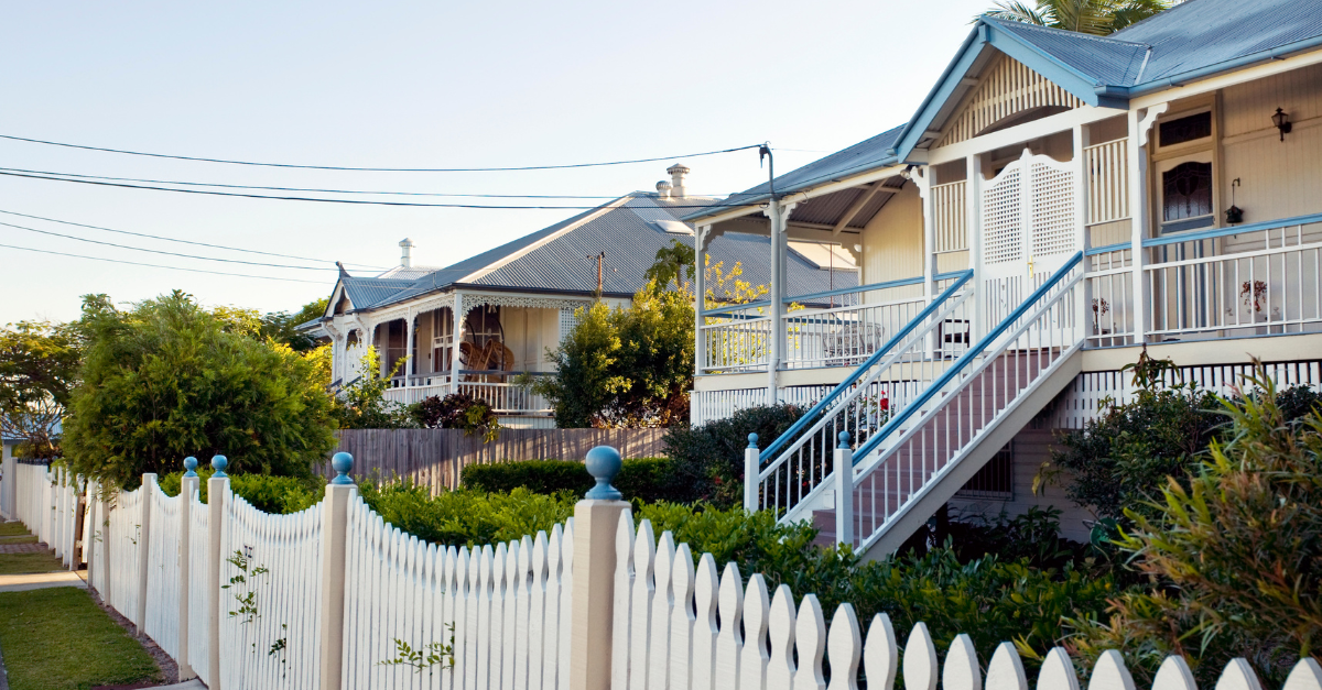 row of queenslander homes sitting behind a white picket fence with green hedges to showcase how the 2025 first home guarantee will impact queensland buyers